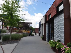 Quiet urban street with brick buildings, decorative tiled walls, greenery, and a partly cloudy sky overhead