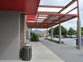 Outdoor shopping plaza with HomeGoods and Walmart stores under red metal canopy and parking lot on a cloudy day
