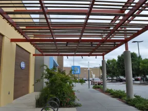 Outdoor shopping area with Ross and Walmart stores, covered walkway, plants, and parked cars on a cloudy day