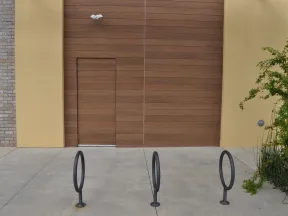 Empty bike racks in front of a modern wooden and yellow building wall with a concealed door and greenery.