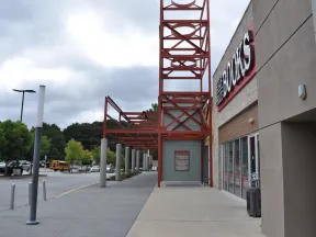 Exterior view of a bookstore entrance with red metal framework and a cloudy sky overhead.