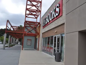Exterior view of Half Price Books store with red metal framework and clear sidewalk under cloudy sky.