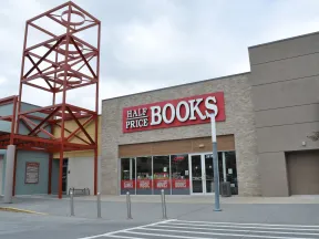 Half Price Books store exterior with large red and white sign and metal architectural feature against a cloudy sky.