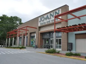Exterior view of JOANN fabrics and crafts store with brick facade and red pergola on a cloudy day