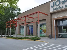 Exterior view of Jo-Ann Fabrics and Crafts store with brick facade and red metal awning structure.