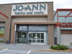 Facade of Jo-Ann Fabrics and Crafts store with glass entrance and exterior signage on a cloudy day