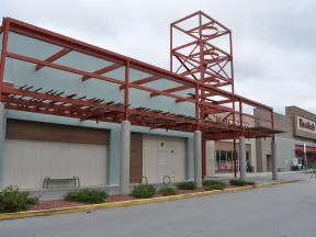 Empty shopping center front with red metal framework and closed store entrances under cloudy sky