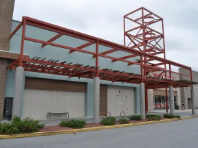 Empty storefront with modern red metal awning structure and overcast sky in a shopping center parking lot
