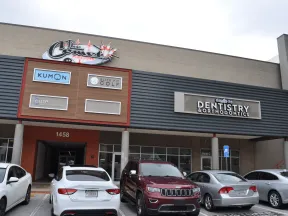 Exterior of a commercial building with signs for Kumon, Elite Golf, dentistry, and parked cars outside