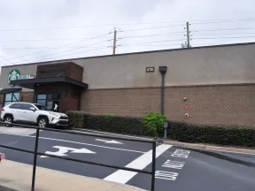 Exterior view of a Starbucks coffee shop with a white SUV parked and directional arrows on the road.