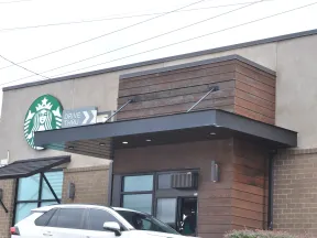 Starbucks coffee shop exterior with drive-thru lane and a white SUV parked nearby during daytime.