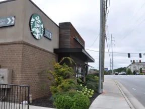 Exterior view of a Starbucks coffee shop with drive-thru signs and a nearby street intersection on a cloudy day