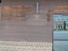Wood-paneled wall with modern light fixture above brick ledge next to reflective glass window showing street view.