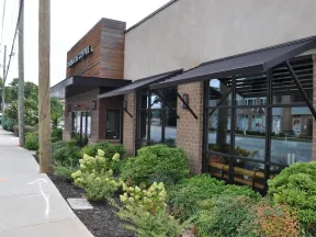 Starbucks Coffee shop exterior with large windows, awnings, and landscaped greenery along the sidewalk.