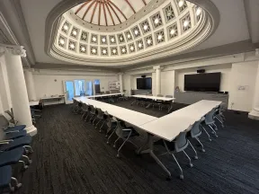 Conference room with U-shaped tables and chairs under a decorative domed ceiling with natural light.