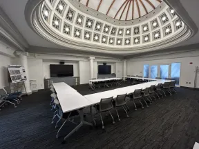 Modern conference room with U-shaped white tables, rolling chairs, and a decorative domed ceiling with lights.