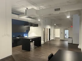 Modern office kitchen area with black island, bar stools, blue accent wall, and open hallway with wood floors.