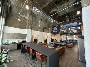 Spacious industrial-style office with high ceilings, lounge areas, kitchen, and multiple seating options under exposed ductwork.