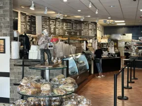 Cozy bakery interior with bread display, glass cases, menu boards, and customer ordering at counter.