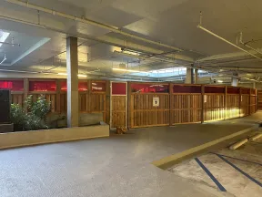 Indoor parking area with wooden privacy partitions and red-tinted upper panels under fluorescent lights