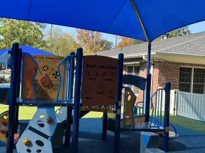 Children's playground with sign language learning panel and colorful climbing structures under a blue shade canopy.