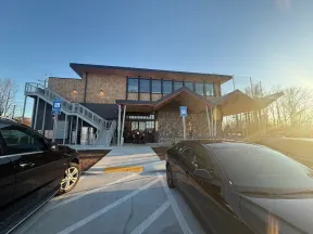Modern two-story building with stone and wood accents, accessible ramps, parked cars, and bright sunset lighting