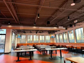 Spacious restaurant dining area with orange booths, wooden tables, black chairs, and large windows with outdoor views.