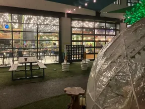 Outdoor dining area with picnic table, clear igloo dome, oversized Connect Four game, and string lights at night