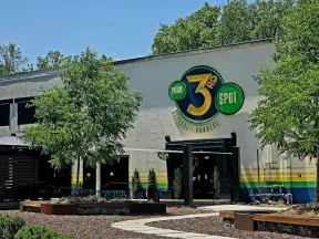 Exterior of a building with a large colorful 3rd Spot logo, surrounded by trees and outdoor seating area.