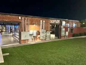 Night view of Scofflaw Brewing Co building with exposed brick, electrical panels, and green lawn in front.