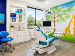 Bright pediatric dental office with blue chairs, nature-themed wall mural, and a dental chair facing a large window.