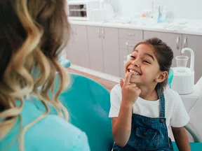 Smiling young girl pointing to her teeth at the dentist during a checkup in a modern clinic.