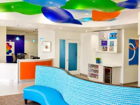 Modern dental office reception with blue curved seating, colorful ceiling decor, and bright artwork on walls.