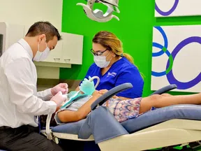 Dentist and assistant wearing masks treating a patient lying on a dental chair in a modern clinic.