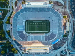 Aerial view of a large football stadium with an empty field and surrounding seating under daylight.
