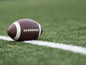 Close-up of a football resting on artificial turf, highlighting texture and field markings.