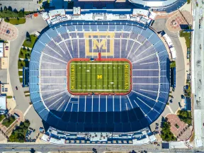 Aerial view of an empty Michigan football stadium with field markings and seating sections visible.