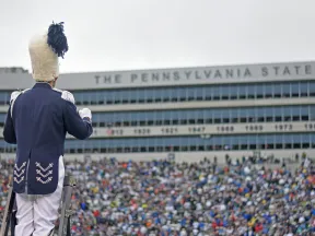 Marching band drum major in uniform leads crowd at Penn State stadium during a game day event.
