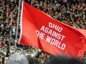 Red flag with Ohio Against The World text waving above a crowd at a sports stadium event.