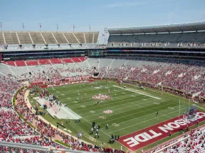 Wide view of a college football stadium with fans, players on the field, and Crimson Tide end zone markings.
