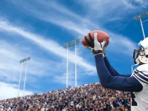A football player catching a ball in a stadium packed with fans under a clear blue sky.
