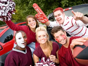 Cheerful group of fans in team colors celebrating at a tailgate party with pom-poms and a football.
