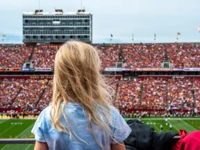 Child watching a football game in a crowded stadium with cheering fans and vibrant team colors.