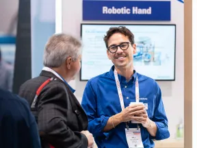 Man in blue shirt explaining robotic hand technology to visitors at a trade show booth
