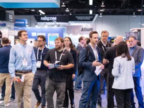 Attendees networking and exploring booths at a busy technology trade show event in an exhibition hall.