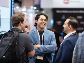 Three men engaged in lively conversation at a professional conference with badges and business attire.