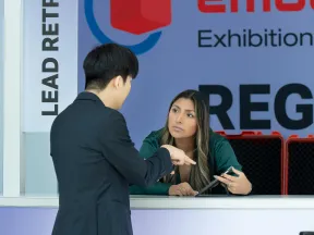 Man in suit discussing with woman at lead retrieval registration counter during exhibition event.
