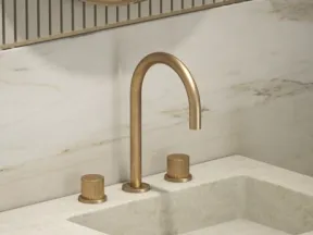 Modern bathroom sink with beige marble countertop and wall, gold faucet, and matching handles beneath round mirror.