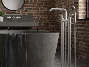 Modern bathroom with gray freestanding stone bathtub, black towel, brick wall, and stainless steel floor-mounted faucet.