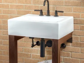 Modern white ceramic sink with black faucet and handles on wooden stand against brick wall.